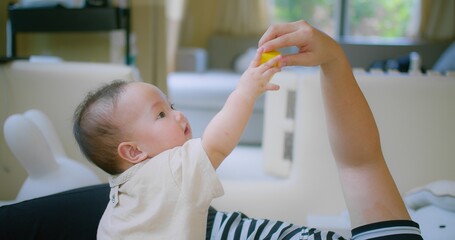 Adorable Asian Baby Reaching for Toy blocks from mother hand in Bright Playroom with Natural Light...