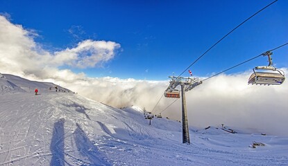 Chairlift over snowy slopes with skiers and clouds in Kleinwalsertal