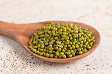 Mung beans in a wooden spoon on beige kitchen table background. Healthy plant-based protein, healthy cooking ingredient for vegan recipes and vegetarian diets, close up, top view