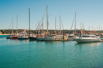 Fototapeta premium Docked sailboats and yachts in a marina with vibrant orange buildings and a clear sky in the background.