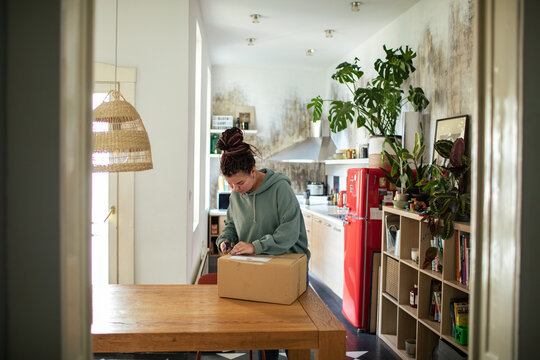 Woman opening package with scissors at home in cozy kitchen