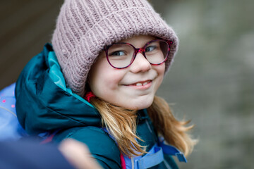 Cute little girl o the way to school. Healthy happy child with eyeglasses walking to primary school. Smiling child with schoolbag on the city street, outdoors. Back to school.