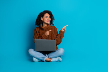 Portrait of a happy young woman with a laptop against a blue background showing with both hands a...
