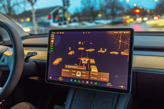 Tesla Model Y interior with touchscreen displaying autopilot visualization, detecting vehicles, traffic lights and surroundings at night. Sweden.