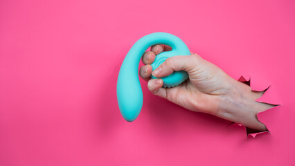 Hand with blue vibrator sticking out through pink paper background. Copy space. 