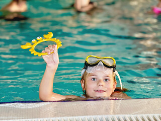 Happy little girl with in swimming pool learning to dive. Little school child with swimm glasses,...