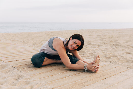 Woman practicing Janu Sirsasana on a beach at sunset