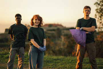 Three young volunteers posing while picking up trash in nature
