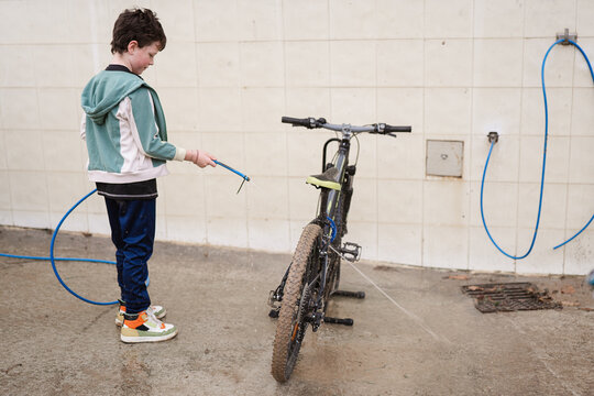 Young Boy Washing Mountain Bike with Hose Outdoors
