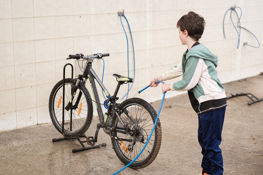 Child washing bicycle with hose in an outdoor setting