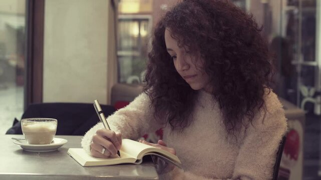 young south american woman handwriting on a block notes sitting in a cafe