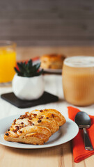 A close-up view of a delightful coffee shop table arrangement, featuring two flaky pastries, a frothy coffee, and a refreshing orange drink.
