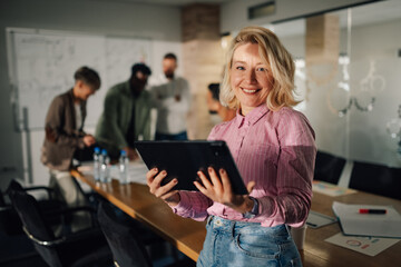 Project manager smiling and holding tablet in busy office