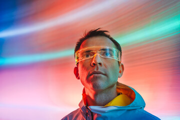 Man wearing glowing futuristic glasses looking up standing in front of neon lights background