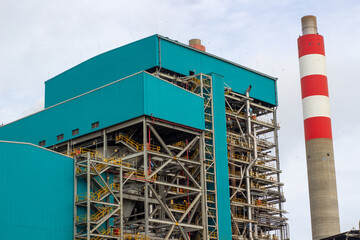 Modern industrial power-plant with teal boiler building and tall striped chimney. Large electricity industry