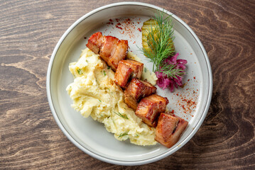 A delicious plate featuring tender grilled meat skewers served over creamy mashed potatoes. Garnished with pickles, red onion, and fresh herbs. Perfect for food photography or culinary use.