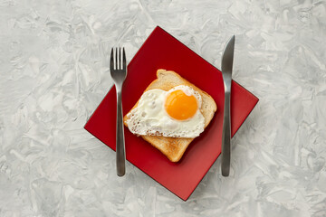 Scrambled eggs on toaster fried bread on quadrangular red plate on  a textured white table, top view.