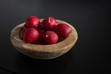 Radishes lying in a wooden bowl on a black background.