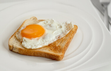 Scrambled eggs on toaster fried bread on quadrangular white textured plate on white table, top view.