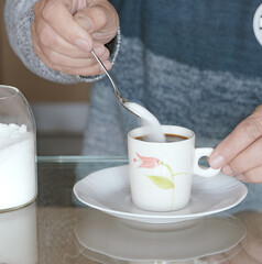 Putting sugar in a cup of coffee on a white plate.