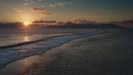 Golden sunset casting a magical glow over a tranquil ocean, with gentle waves lapping at the shore and majestic mountains rising in the background, evokes serenity