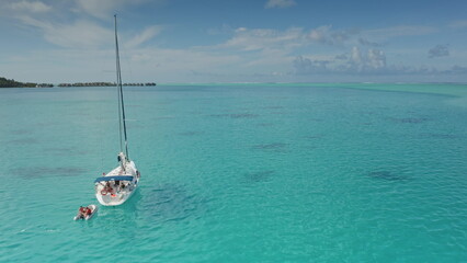 Tourists enjoying a sailing adventure in the turquoise lagoon of Bora Bora, gliding past overwater bungalows under a bright sky, capturing the essence of tropical paradise in French Polynesia