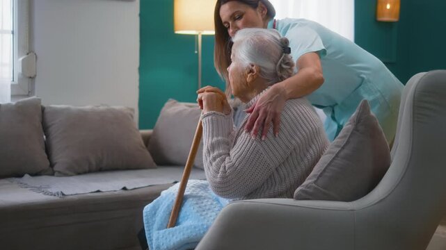 Kindness female caregiver hugs a senior woman sitting in an armchair, the concept of kindness care, and homecare for retired old people at home. Senior care, medical service, nursing home.