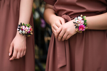 Close-up of two women in mauve dresses wearing delicate floral wrist corsages. The flowers are...