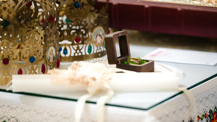 Close-up of wedding rings nestled in a small wooden box.  Ornate gold crowns are visible in the...