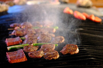 Close-up of sausages and meatballs cooked on a barbecue in a meat restaurant. Smoke comes out of the barbecue. Meat prices. Barbecue pleasure. Weekend picnic.