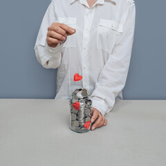 Flying red heart in transparent jar with silver coins. Concept of doing good. Woman in white shirt,...