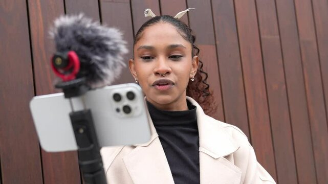 Young female reporter recording a video blog using a smartphone and external microphone, captured in slow motion