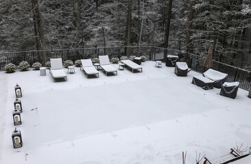 snow covered lounge chairs surrounding a shuttered swimming pool in winter (looking down aerial) back yard patio blizzard snowy weather outdoor furniture cover covered in ground built in off season 