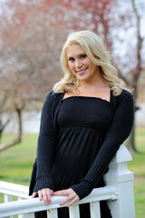 Attractive blonde woman wearing black dress stands in gazebo