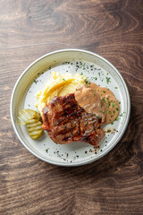 A delicious plate featuring a grilled steak served on creamy mashed potatoes, accompanied by a rich sauce and pickle slices. Perfect for food-related projects and menus.