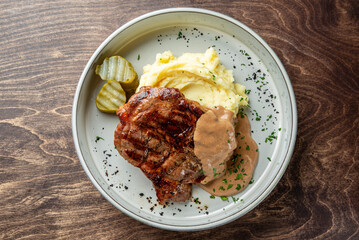 A delicious plate featuring a grilled steak served on creamy mashed potatoes, accompanied by a rich sauce and pickle slices. Perfect for food-related projects and menus.