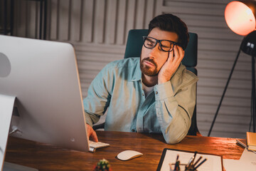Young businessman working late in the office, wearing glasses, feeling tired and stressed,...