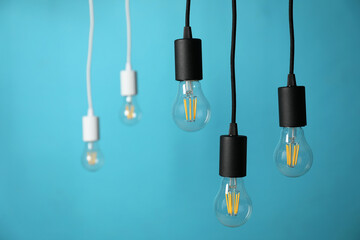 Light bulbs hanging on cords against blue background, selective focus