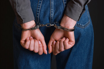 Woman in metal handcuffs on black background, closeup