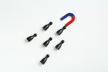 Magnet attracting black game pieces on white background, flat lay