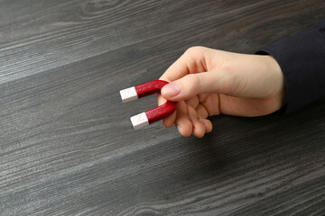 Woman with horseshoe magnet on wooden background, closeup