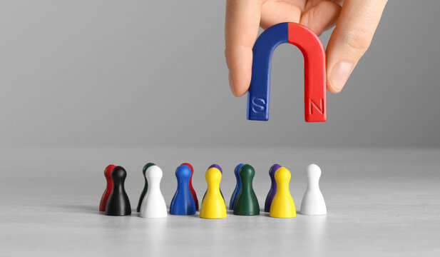 Woman with magnet attracting colorful game pieces at light table, closeup
