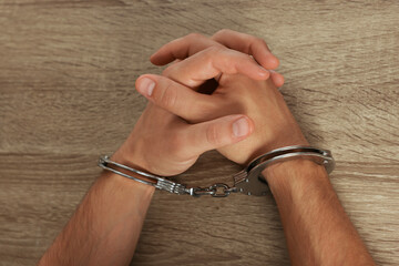 Man in metal handcuffs at wooden table, top view