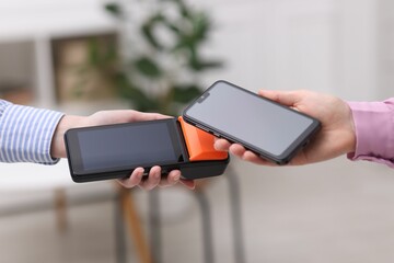Woman paying with smartphone via terminal against blurred background, closeup