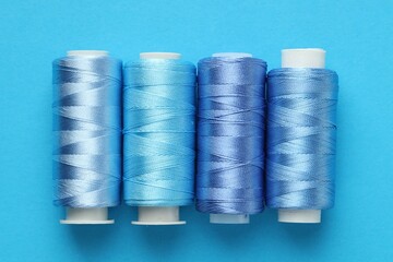 Spools of sewing threads on light blue background, flat lay