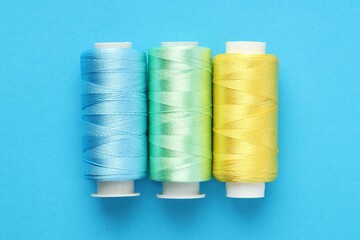 Different spools of sewing threads on light blue background, flat lay