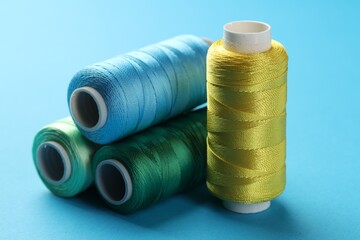 Different spools of sewing threads on light blue background, closeup