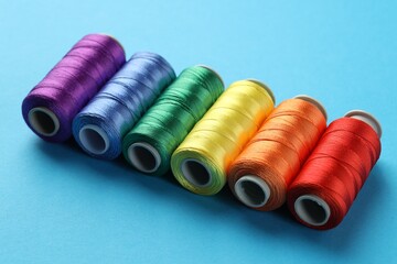 Different spools of sewing threads on light blue background, closeup