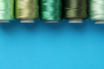 Different spools of sewing threads on light blue background, flat lay. Space for text