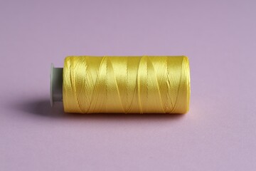 Spool of yellow sewing thread on violet background